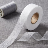 White sheer mesh ribbon roll with a gold-toned cardboard core, shown with a length unspooled on a gray textured fabric background. A spool of gray ribbon is blurred in the background.